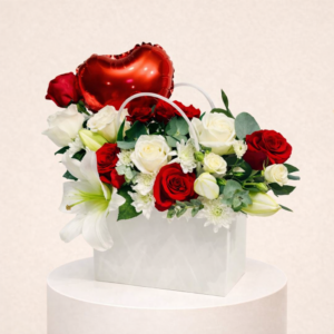 A chic white bag filled with a blend of white and red roses, accented with a few delicate white baby roses, and paired with a vibrant red heart-shaped foil balloon.